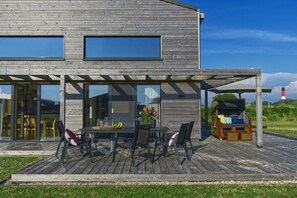 A modern house with a wooden deck, a covered outdoor seating area, and a view of the sea. - Holiday home in Pellworm with swimming pool (Pellworm)
