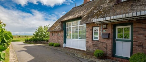 A traditional brick house with a thatched roof, a white door, and a small garden.