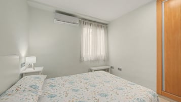 Una camera da letto con un letto, un comodino con una lampada, un condizionatore d'aria, una finestra con tende e un armadio in legno.