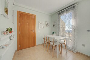 Un comedor con puerta de madera, paredes blancas y una ventana con cortinas de encaje.