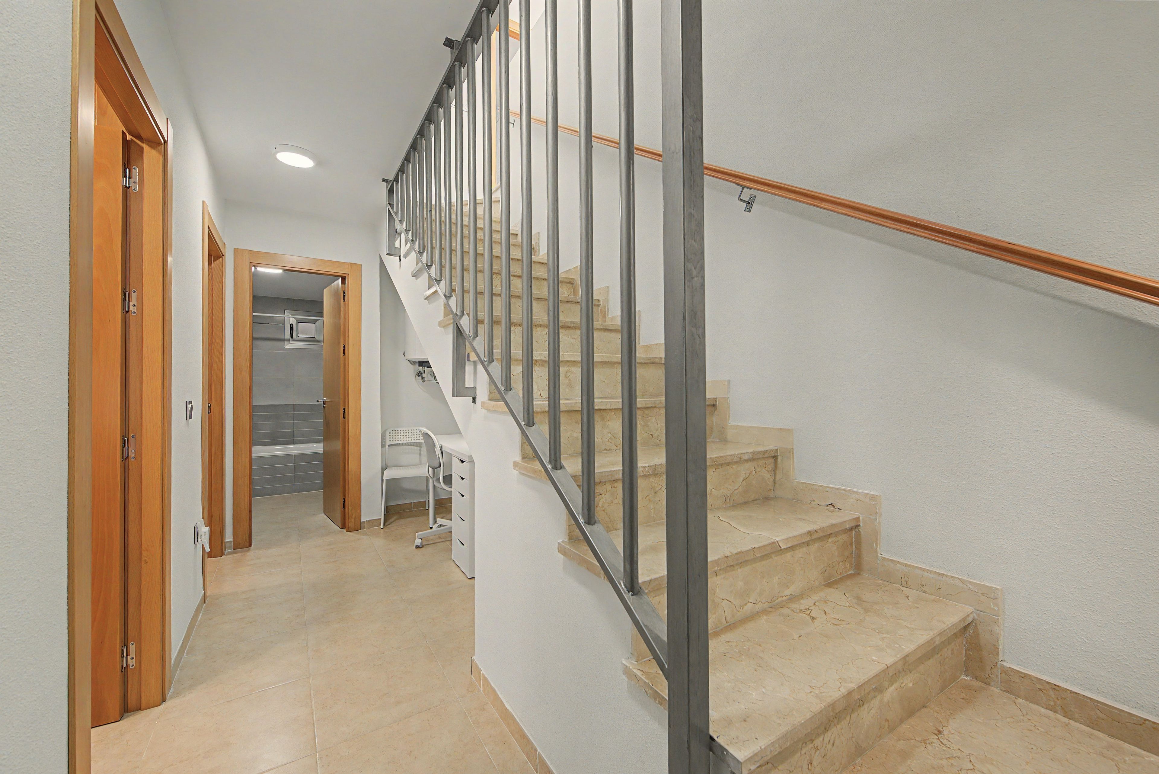 A staircase with a metal handrail and wooden steps, leading to a room with a white wall and a door.