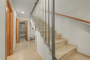 Una escalera con barandilla de metal y peldaños de madera, que conduce a un cuarto con pared blanca y una puerta.