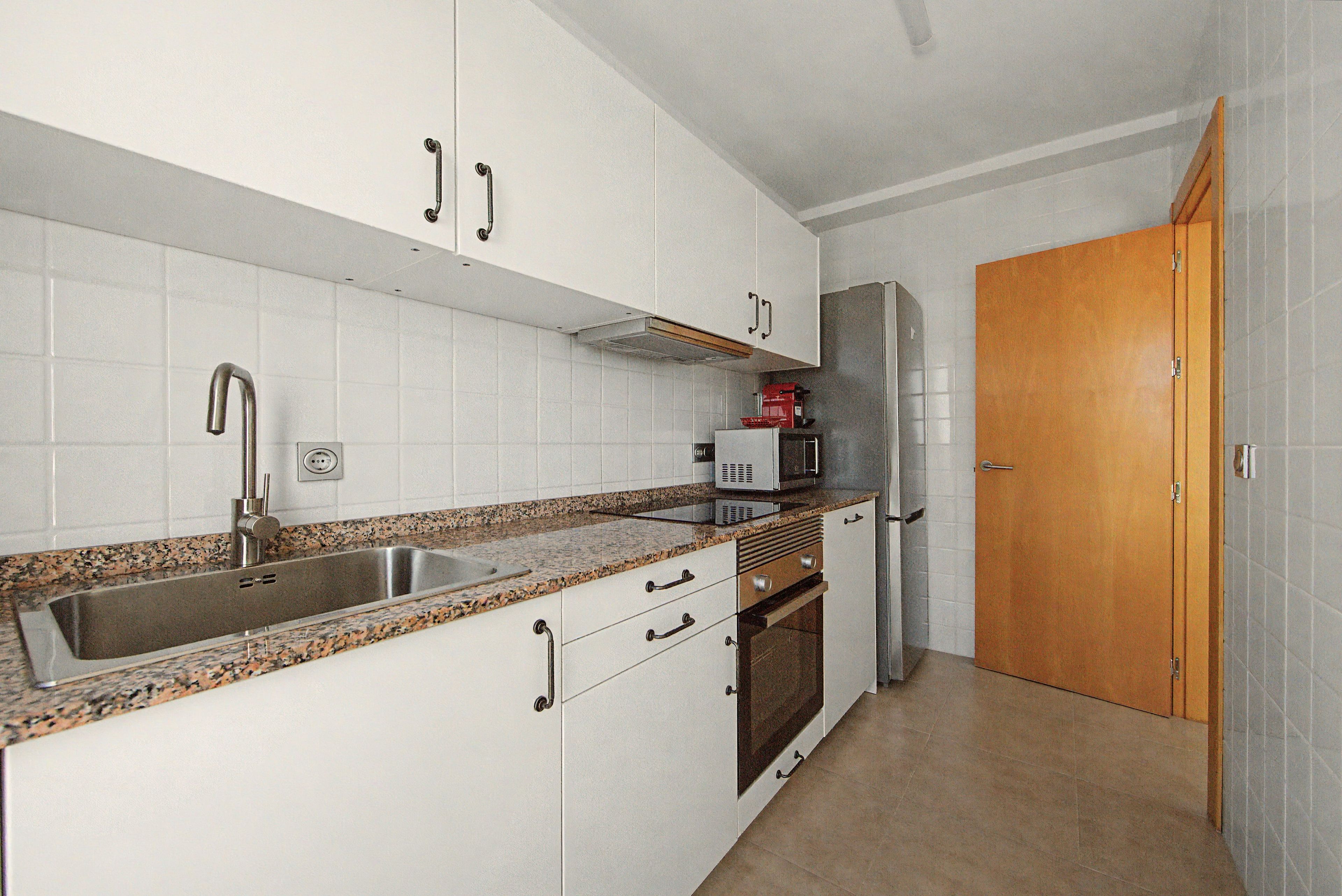 A kitchen with white cabinets, a stainless steel sink, a microwave, and a wooden door.