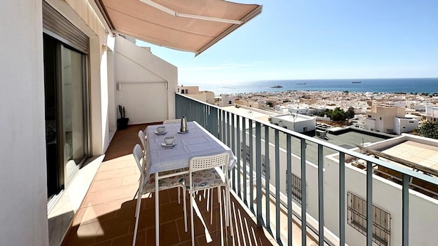 Varanda com mesa e cadeiras, com vista para o centro urbano costeiro.