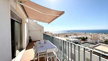 Un balcón con mesa y sillas, con vistas a un paisaje urbano costero.