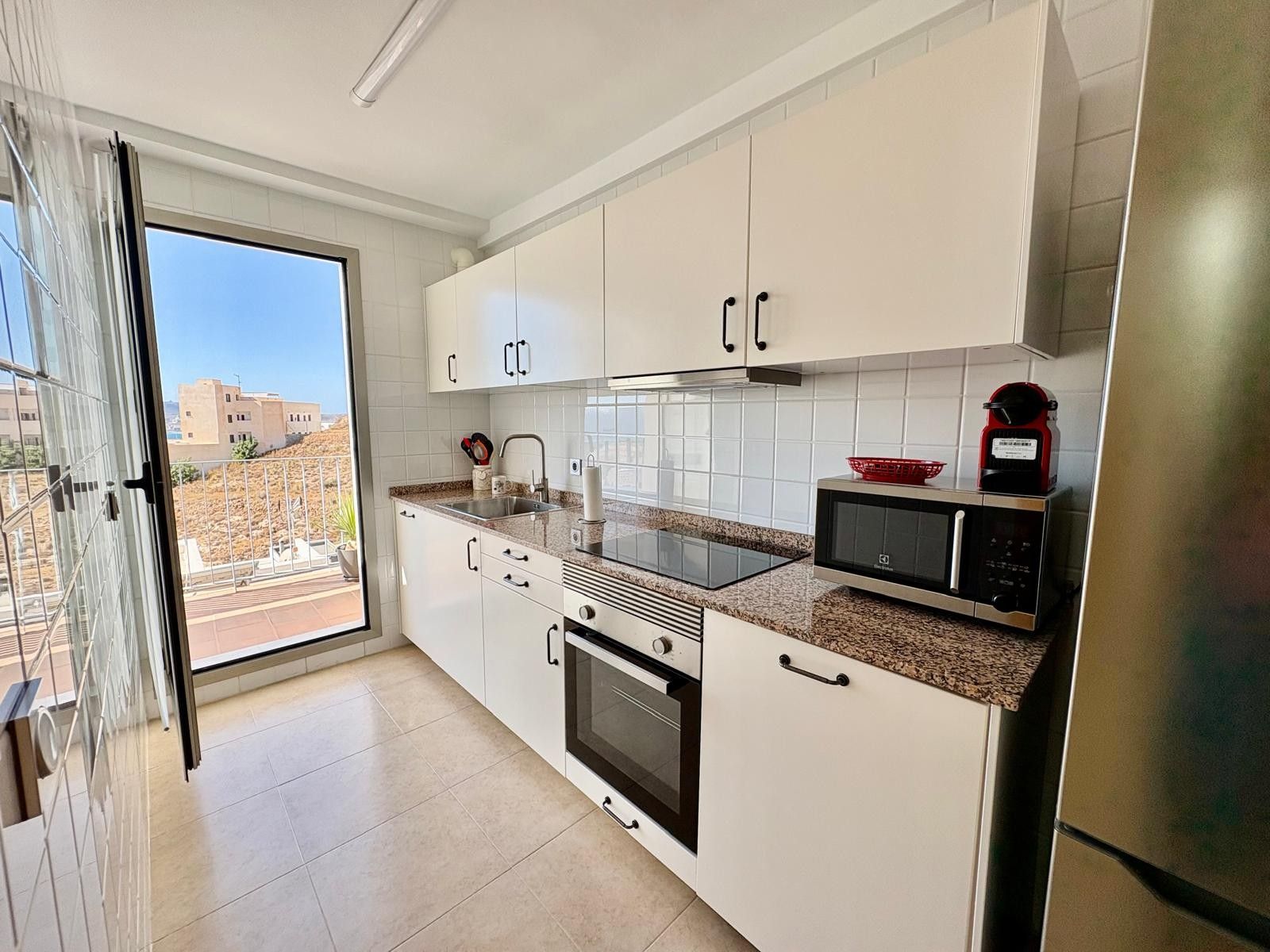 A modern kitchen with white cabinets, a stainless steel refrigerator, a microwave, and an oven.