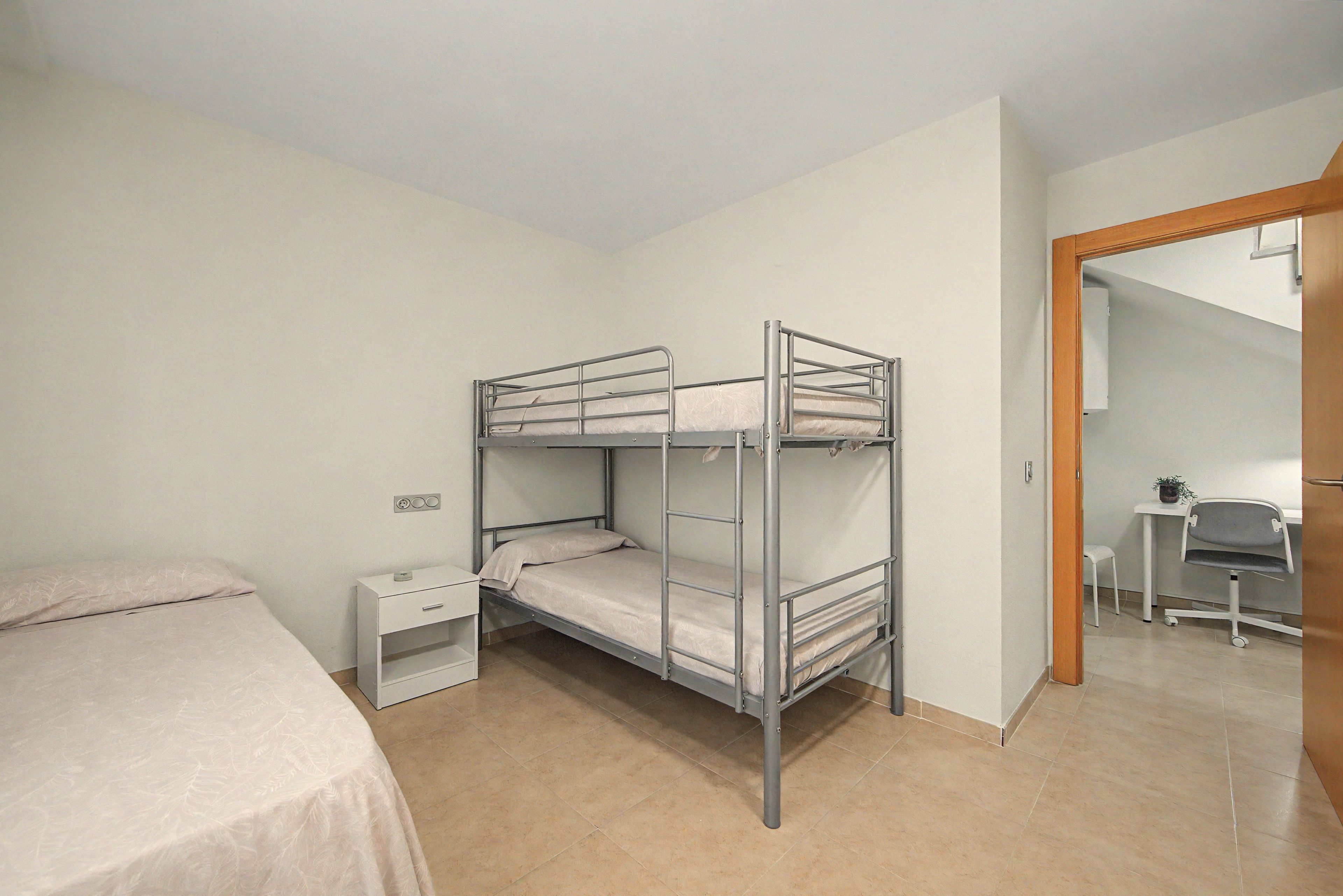 A bunk bed room with a desk and chair, a small bedside table, and a mirror.