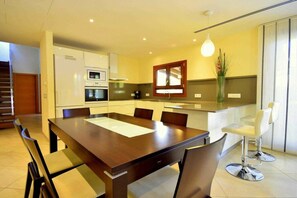 Une cuisine moderne avec un coin repas, comprenant une grande table et des chaises en bois, un four encastré et un réfrigérateur.