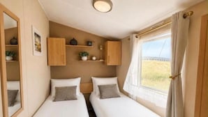 Habitación doble con dos camas, un espejo, una estantería con adornos y una ventana con cortinas.