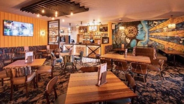 Un restaurante con mesas y sillas de madera, una zona de bar y un mural en la pared.