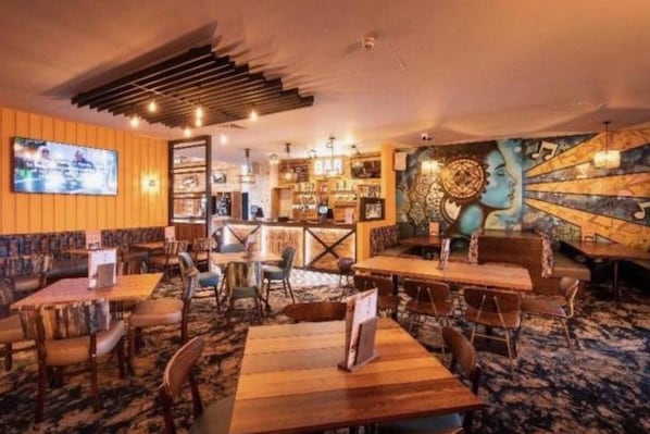 A restaurant with wooden tables and chairs, a bar area, and a mural on the wall. - Seaside Escape at St Osyth (Clacton-on-Sea)