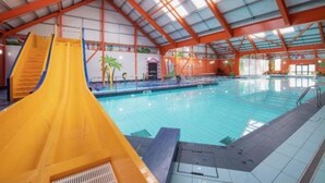Una piscina interior con un tobogán amarillo y un techo alto con tragaluces.