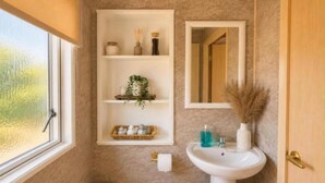 Un baño con ventana, lavamanos, espejo y repisas con artículos de tocador.