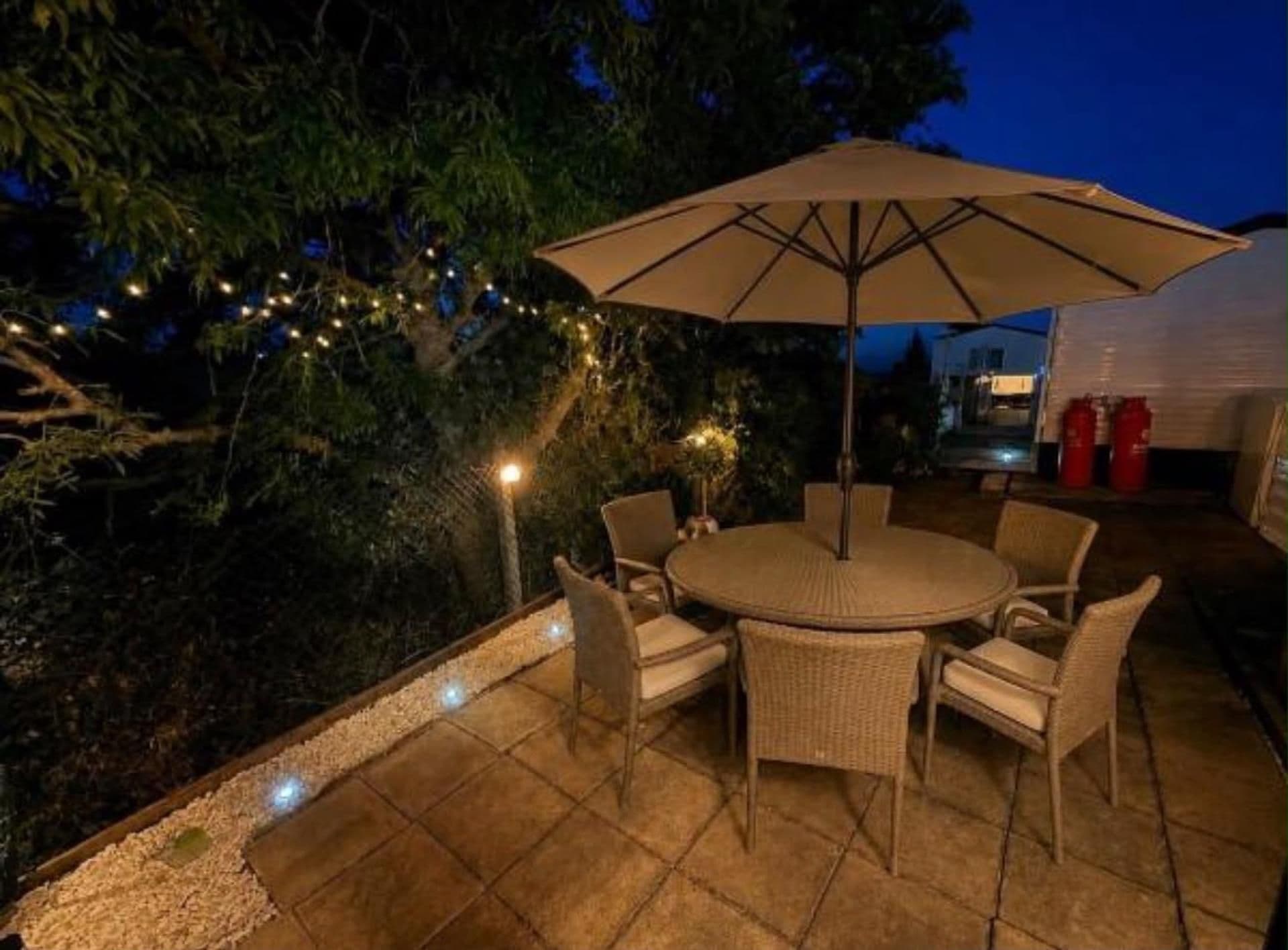 An outdoor patio with a round table and chairs, surrounded by a low wall and string lights.