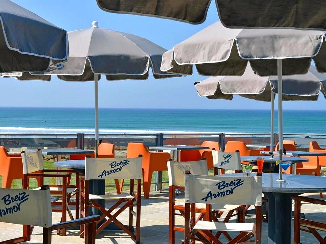 Outdoor seating with umbrellas and tables, chairs with signage, and a view of the ocean.