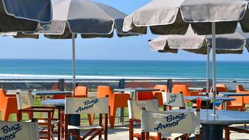 Outdoor seating with umbrellas and tables, chairs with signage, and a view of the ocean.