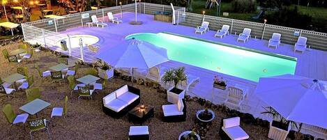 A swimming pool area with lounge chairs and tables, surrounded by a fence and trees.