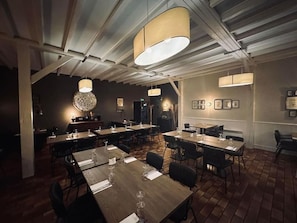 Un restaurante con varias mesas y sillas, iluminación colgante y cuadros en las paredes.
