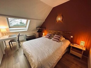Un dormitorio con techo inclinado, una cama con ropa de cama a rayas, un escritorio con silla y una ventana.