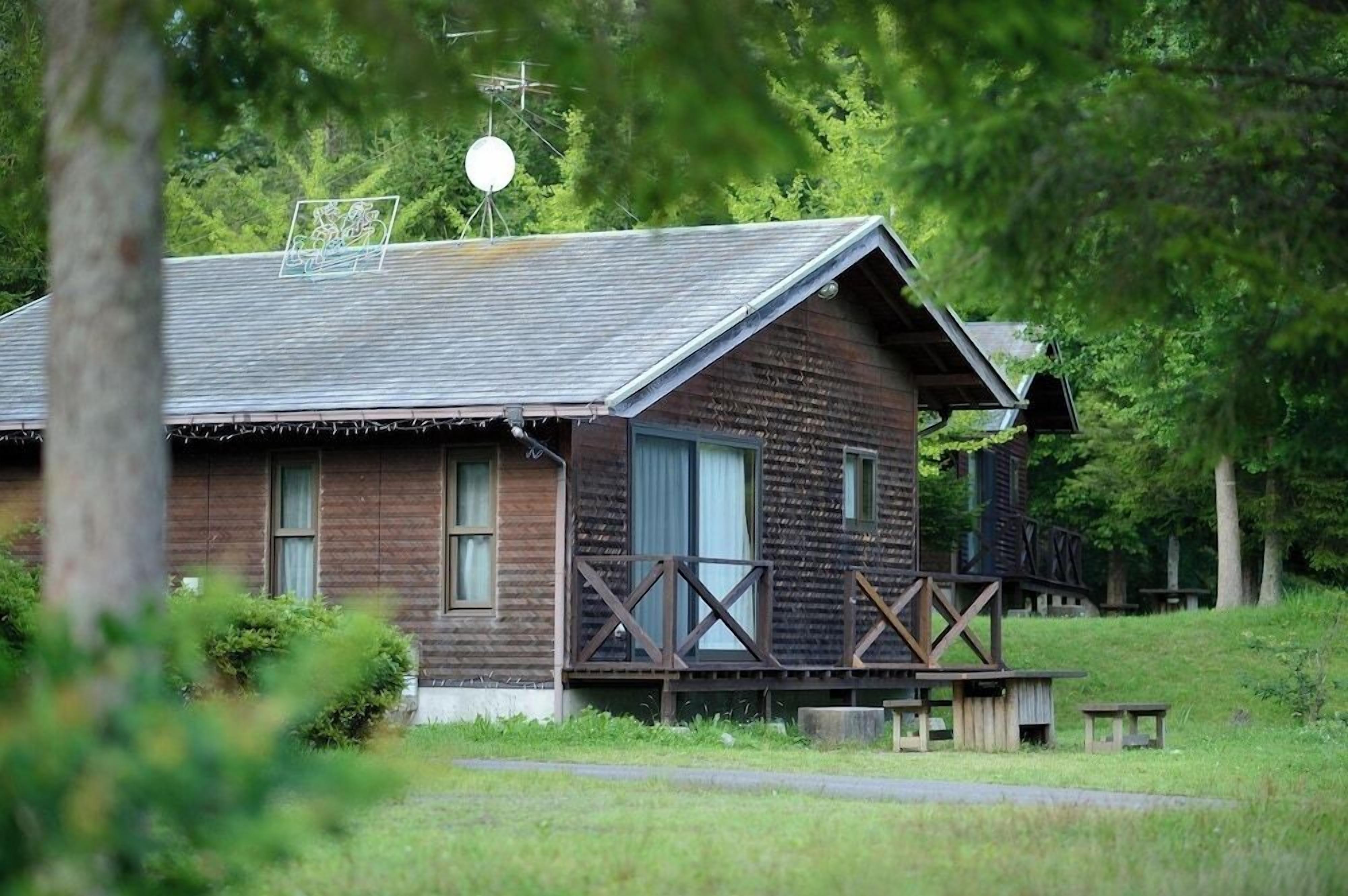 A rustic wooden cabin with a porch, surrounded by greenery.