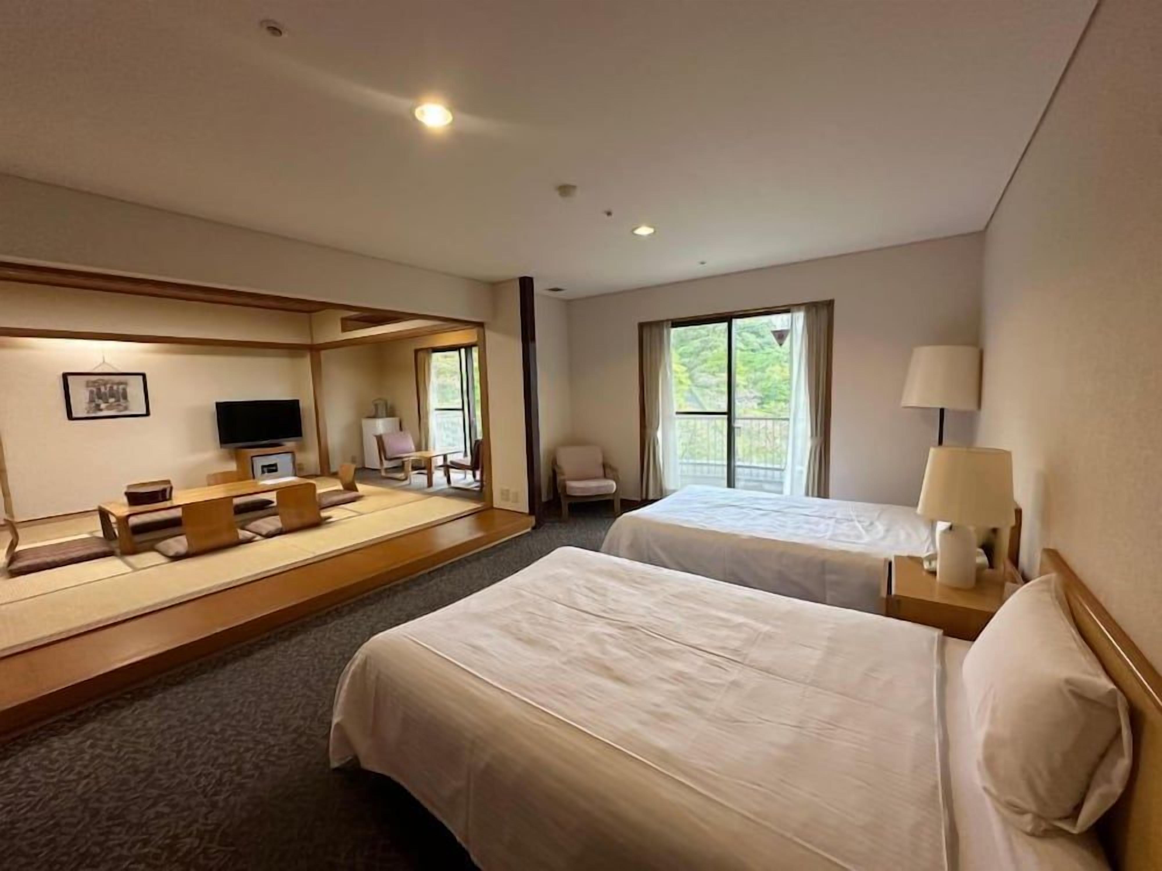 A hotel room with two beds, a television, a desk with a chair, and a window with a view.