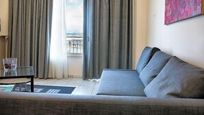 A living room with a sofa, a glass coffee table, and a view of a body of water through curtains. - Hara (Chalcis)