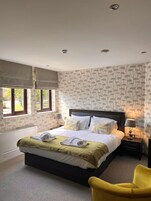 A bedroom with a large bed, two bedside tables, a chair, and a window with curtains.