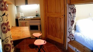 Cocina compacta con estufa, horno y microondas, una puerta de madera y una mesa pequeña con dos sillas rosas.