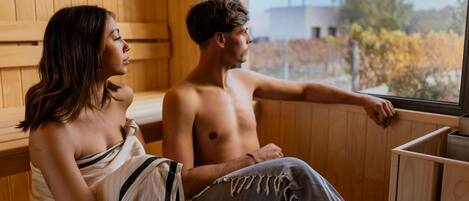 Two people sitting in a sauna with wooden walls and a window.