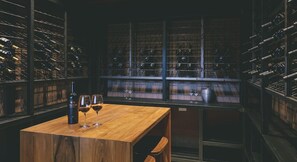 Una bodega con estantes de madera y una mesa con botellas de vino y copas.