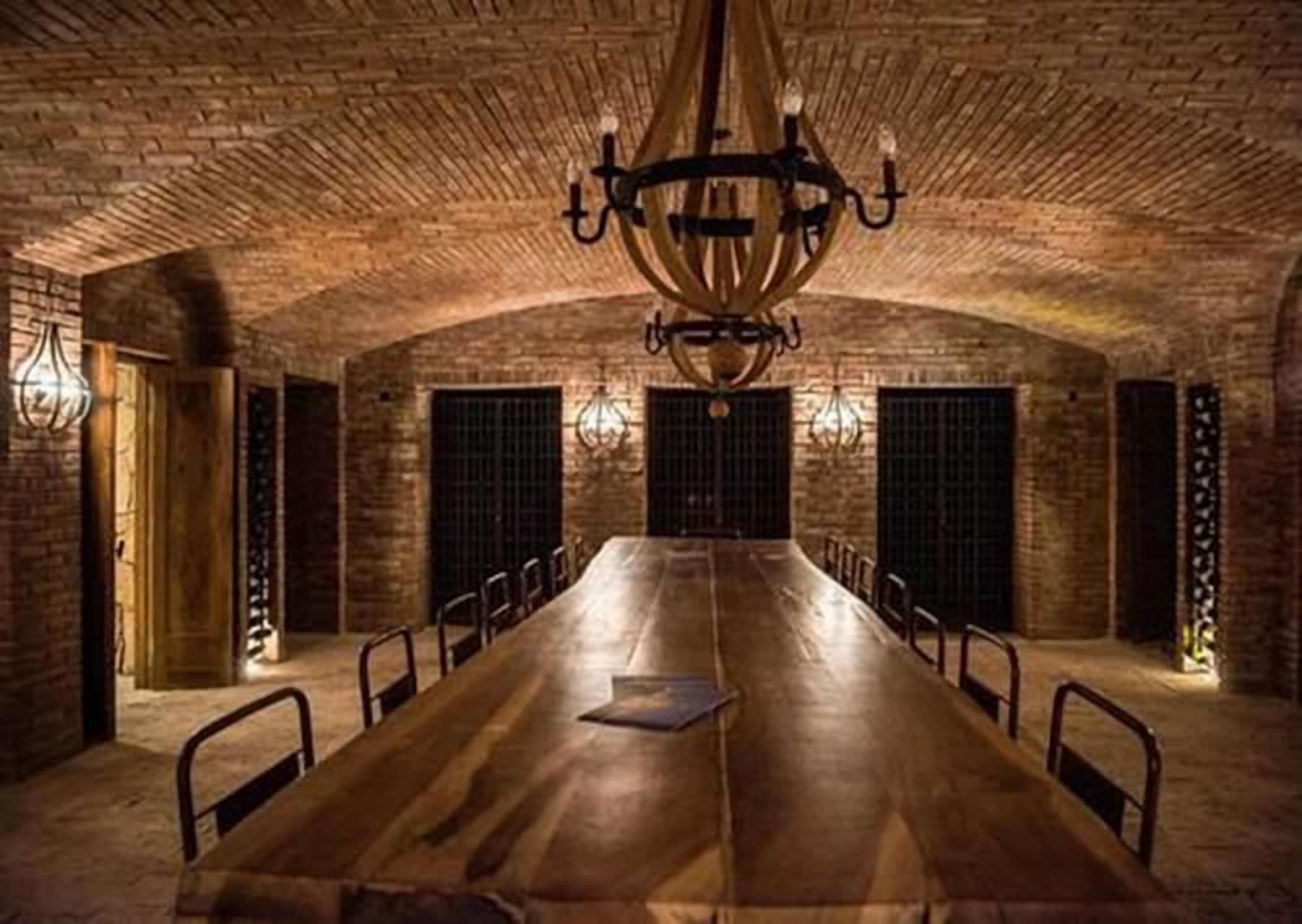 A long wooden table with chairs, a chandelier, and brick walls.