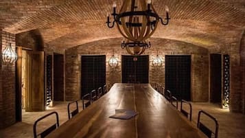 A long wooden table with chairs, a chandelier, and brick walls.