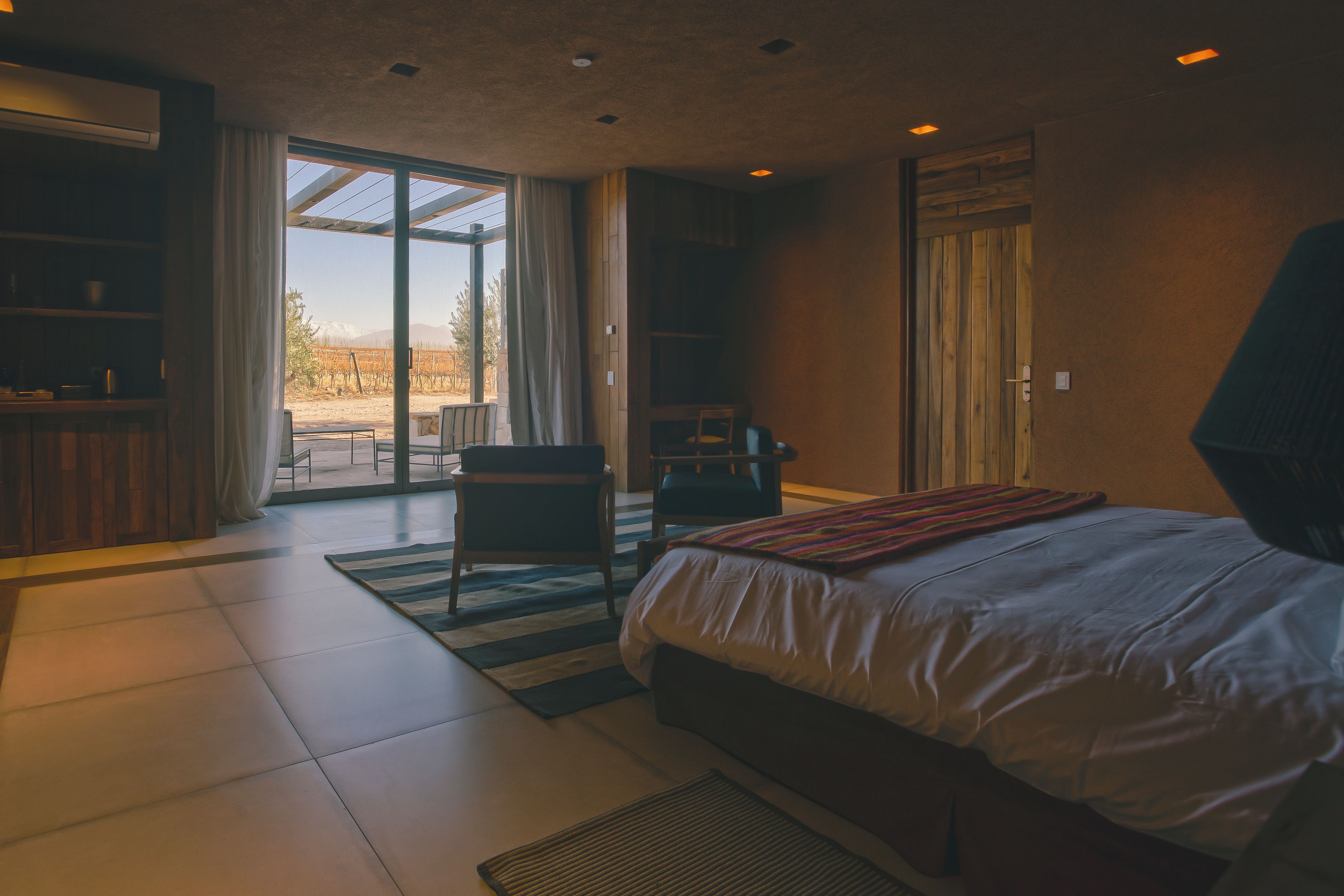 Ein modernes Schlafzimmer mit einem großen Bett, einem Schreibtisch und einem Stuhl. Eine Glastür führt zu einem Außenbereich.