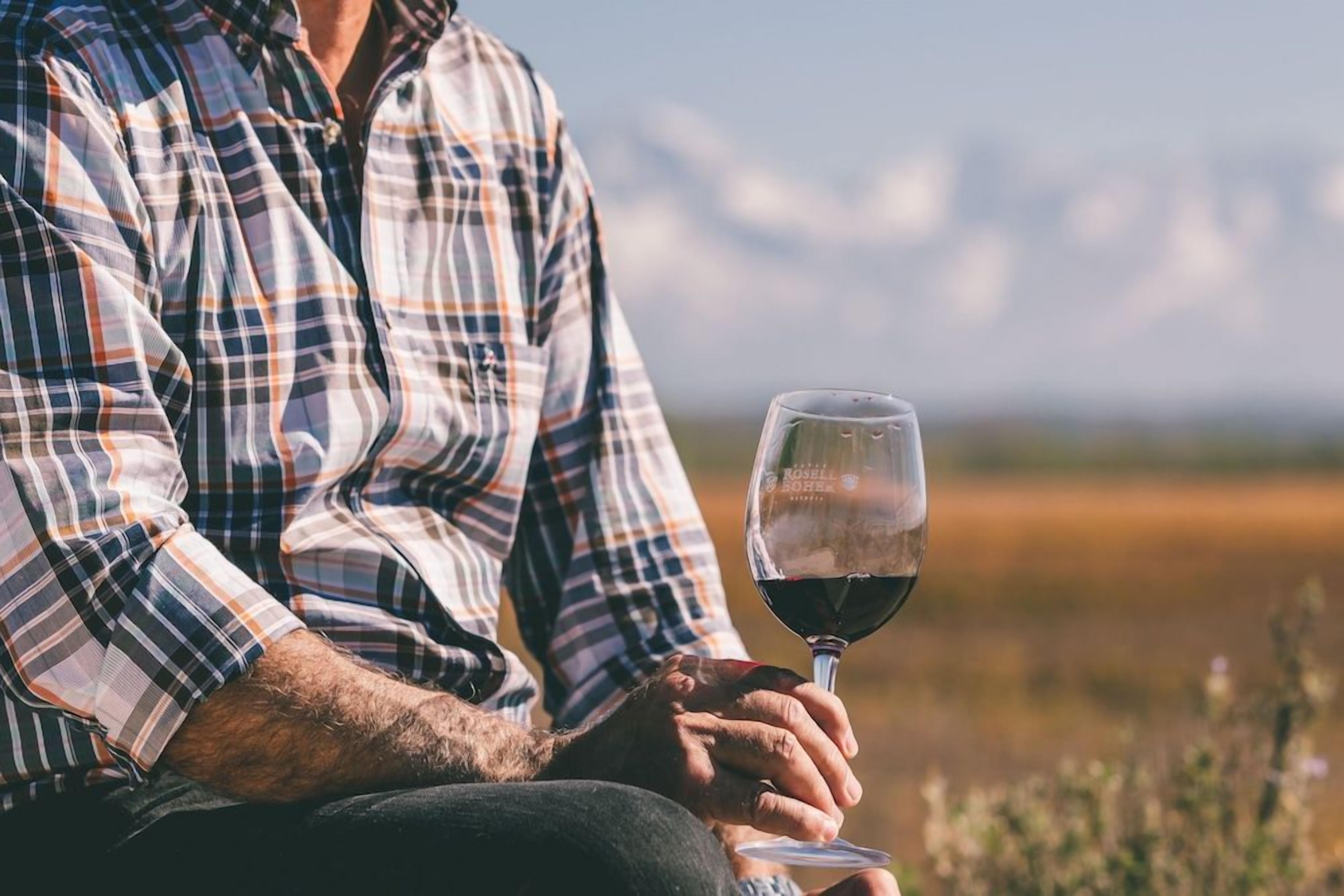 Une personne assise à l’extérieur, tenant un verre de vin.