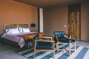 Un dormitorio con una cama, dos sillas, una mesita de noche y una puerta de madera.