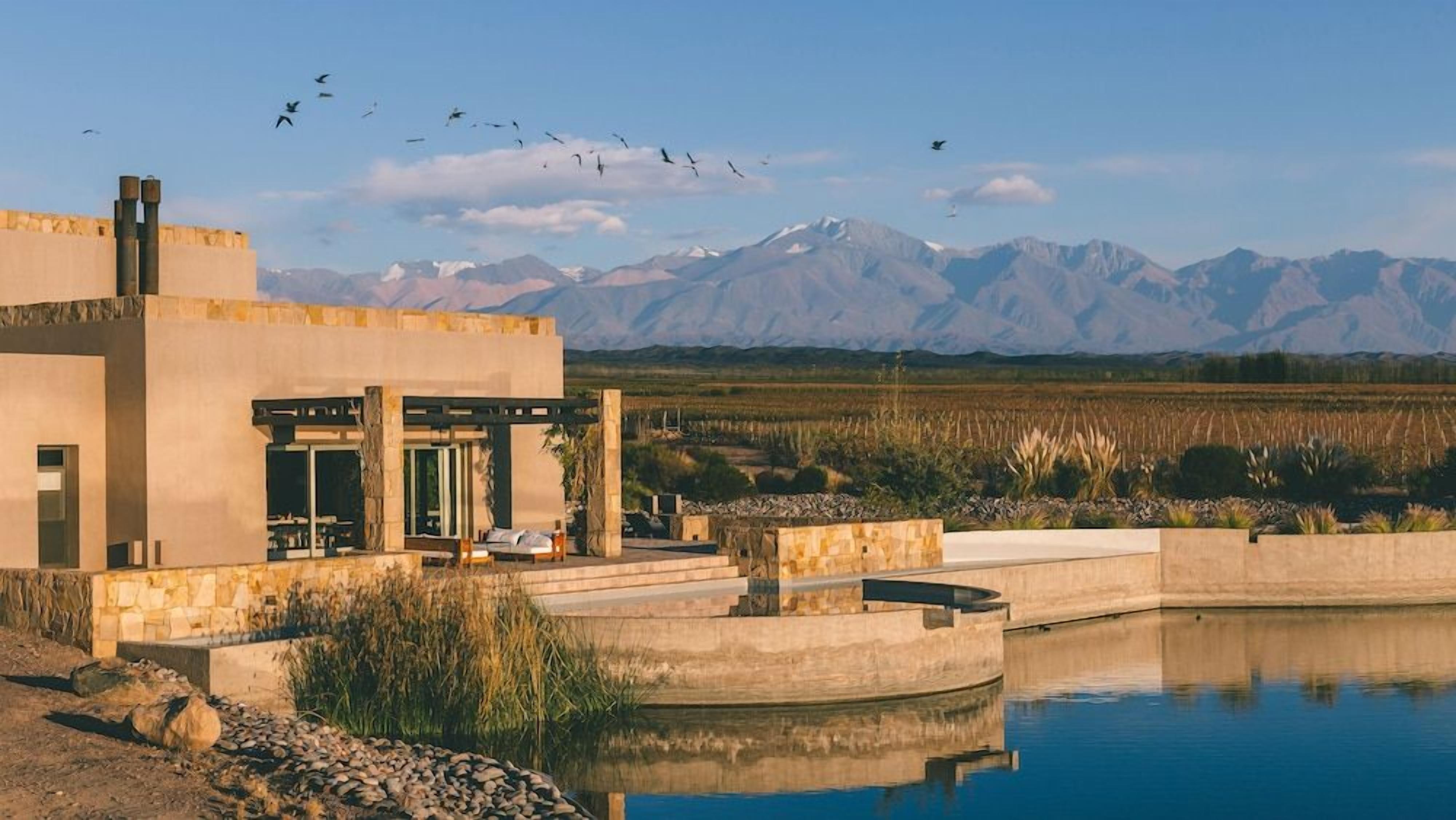 A modern building with a pool, surrounded by a natural landscape with mountains in the background.