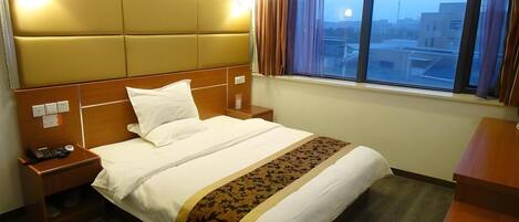 A hotel room with a bed, bedside tables, a desk, and a window with curtains.