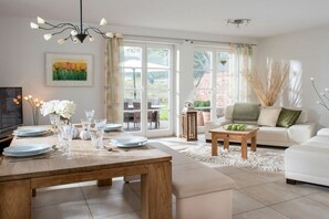 A modern living room with a dining table set for six, a sofa, and a TV. - Holiday home with 1 bedroom (St. Peter - Ording)