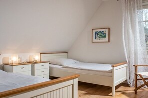A bedroom with two single beds, a bedside table with lamps, a chair, and a framed picture on the wall. - Holiday home with 1 bedroom (St. Peter - Ording)