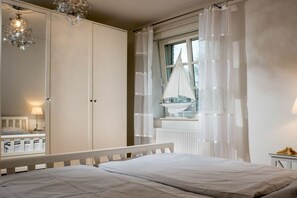 A bedroom with a bed, a wardrobe, a window with curtains, and a small table with a lamp. - Holiday home with 1 bedroom (St. Peter - Ording)