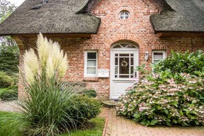 A brick house with a thatched roof, a white door, and a small circular window above the door. - Holiday home with 1 bedroom (St. Peter - Ording)