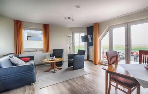 A modern hotel room with a sofa, chairs, a dining table, and a TV. - Holiday apartment with 1 bedroom (Cuxhaven)