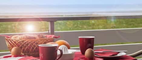 A breakfast table with a basket, eggs, a bowl, and a red cup, set on a balcony with a view.