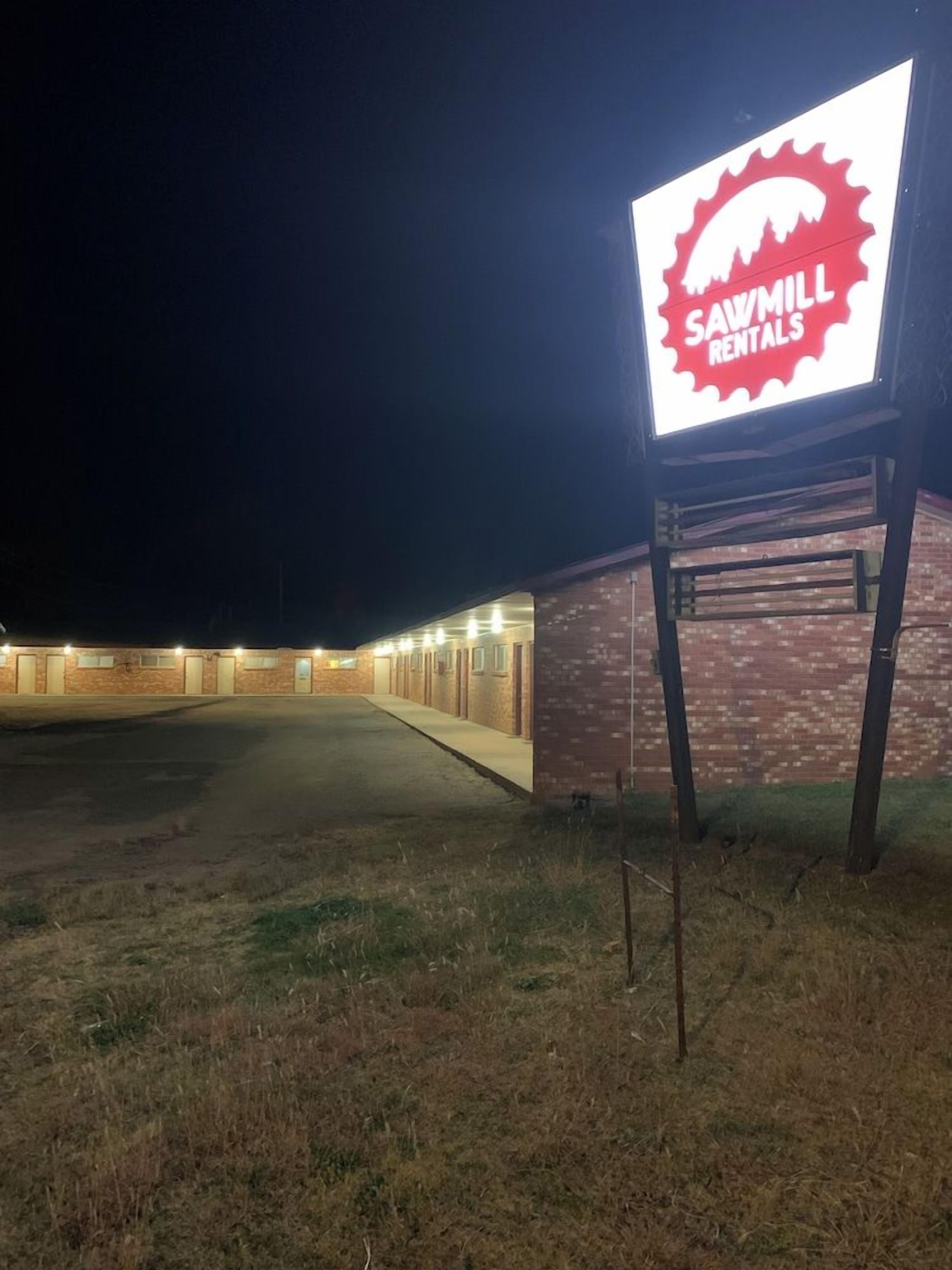 A building with a sign for Sawmill Rentals, featuring a brick facade and a parking lot.