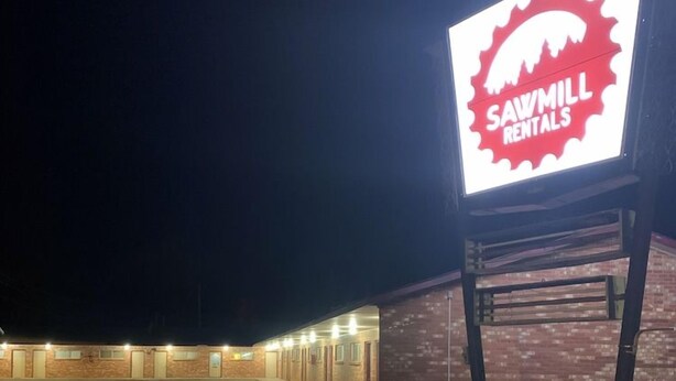 A building with a sign for Sawmill Rentals, featuring a brick facade and a parking lot. - Sawmill Inn (Hennessey)