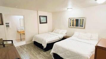A hotel room with two beds, a desk, a chair, a small table, and a trash bin.