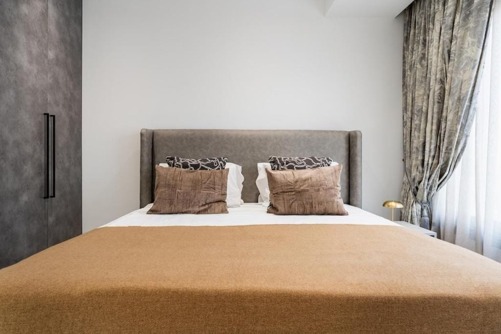A modern bedroom with a large bed, two pillows, a headboard, and a window with curtains.