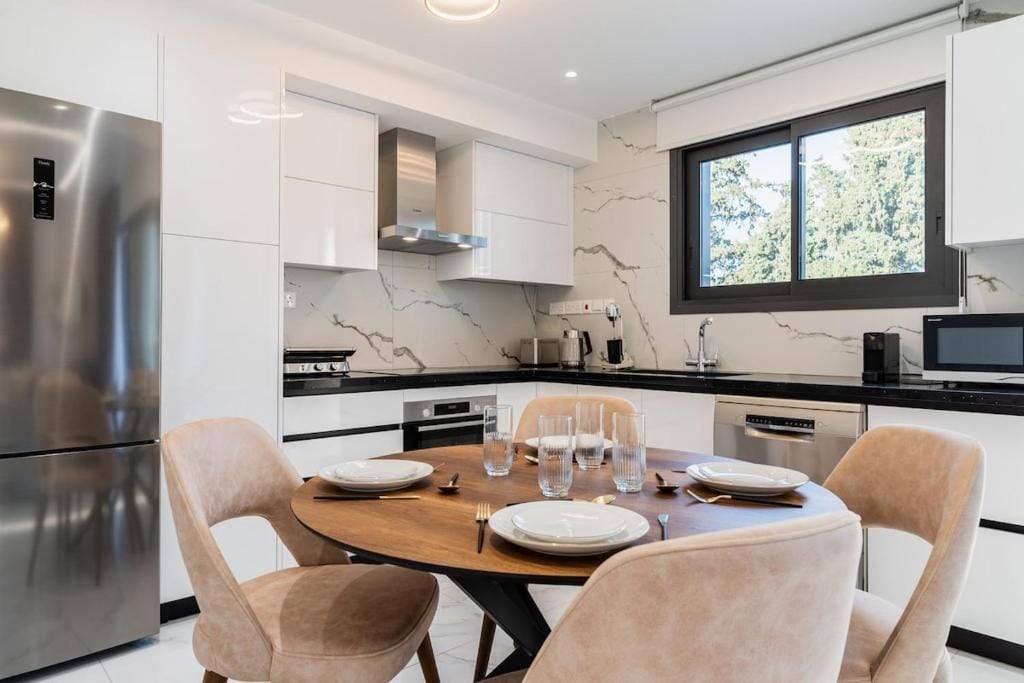 A modern kitchen with white cabinetry, a marble backsplash, and a dining area with a wooden table and cushioned chairs.