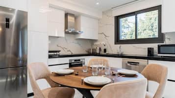 A modern kitchen with white cabinetry, a marble backsplash, and a dining area with a wooden table and cushioned chairs.