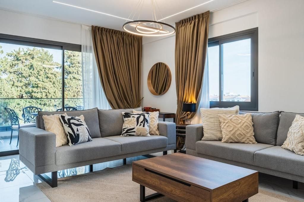 A modern living room with two grey sofas, a wooden coffee table, and a large window with curtains.